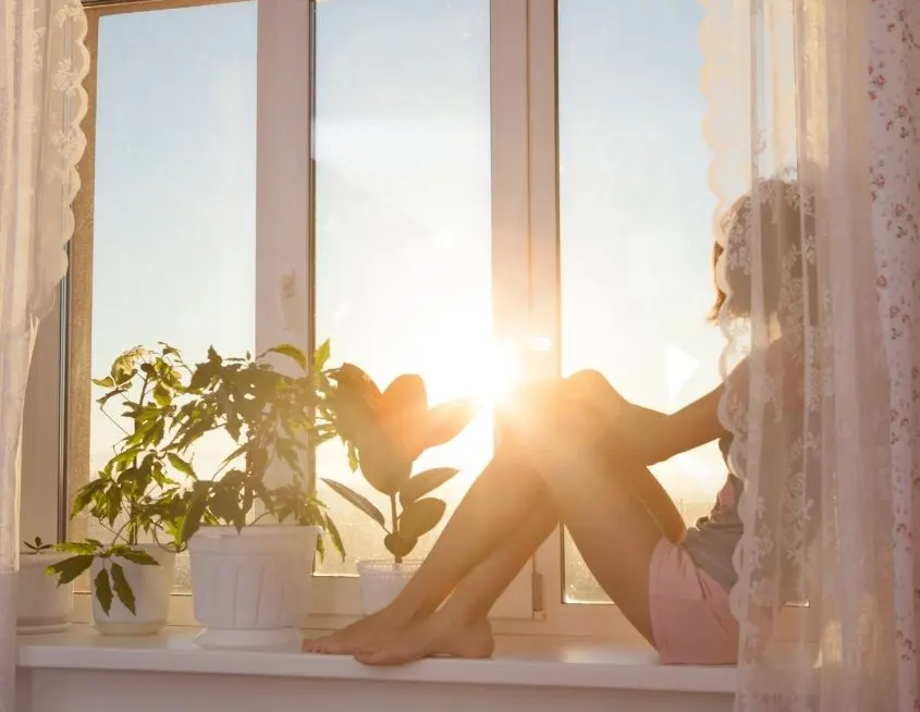 Mujer sentada en la ventana disfrutando de un amanecer quiropráctico Badalona