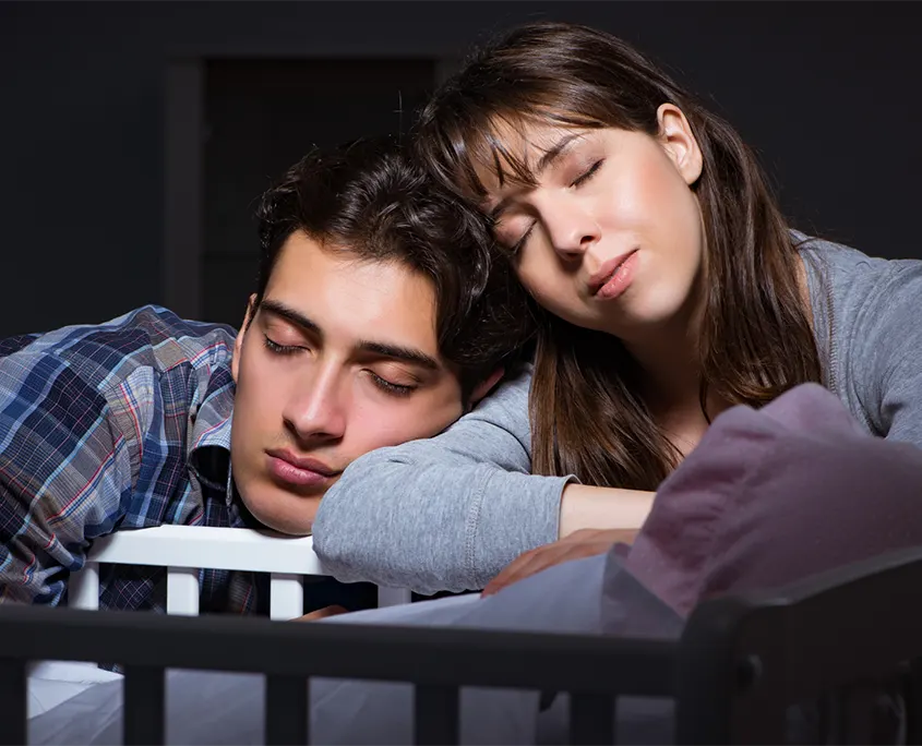 imagen de una pareja que se ha quedado dormida delante de la cuna de su bebé