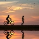 foto de gente corriendo y yendo en bicicleta por la playa con fondo de puesta de sol