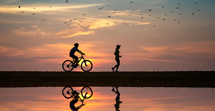 foto de gente corriendo y yendo en bicicleta por la playa con fondo de puesta de sol