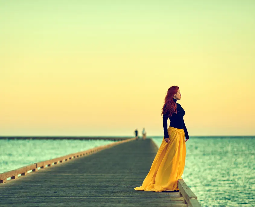 Mujer caminando por un embarcadero de madera mirando al mar