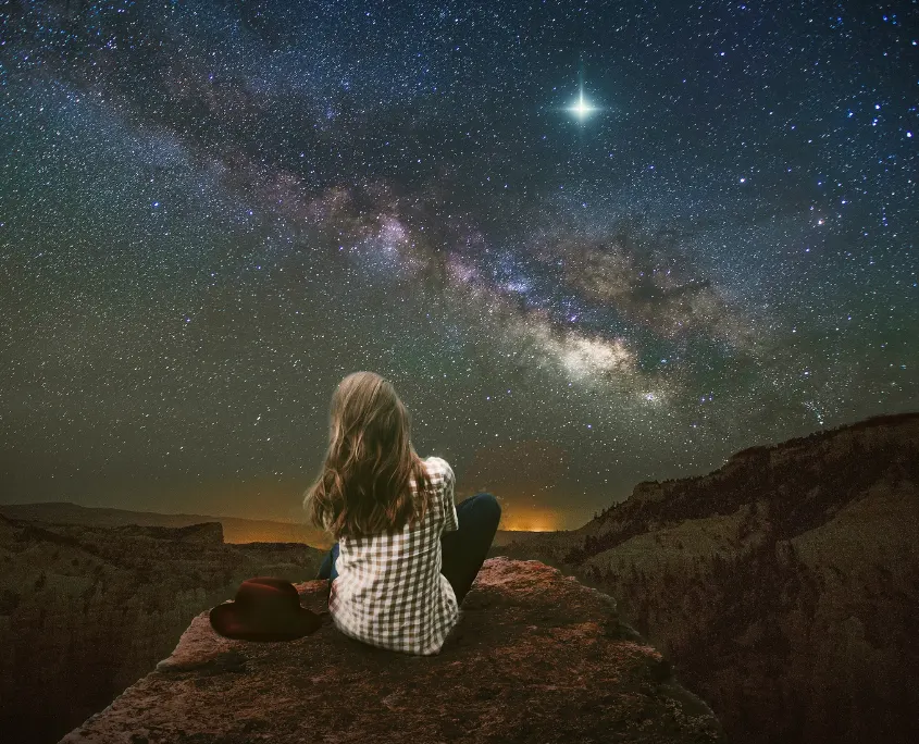 Foto de mujer sentada mirando a las estrellas en plena naturaleza