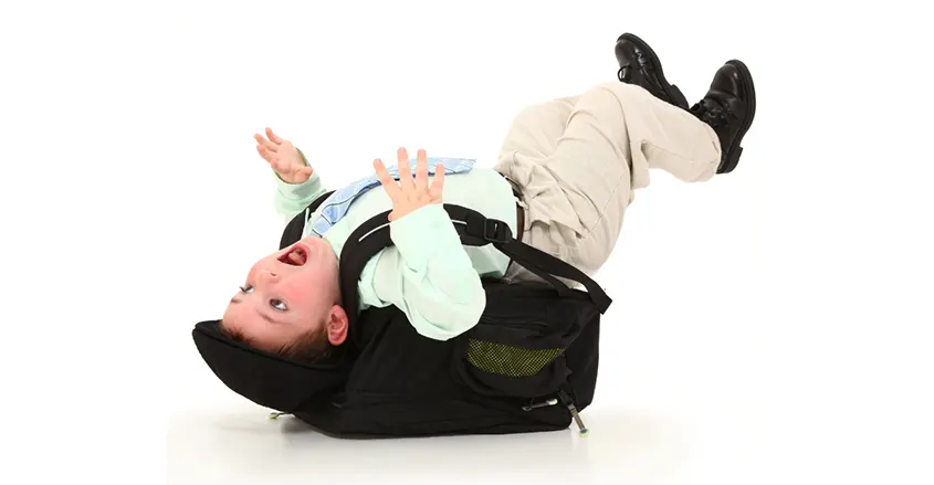 Niño que se ha caído porque le pesa demasiado la mochila para ir al colegio. 