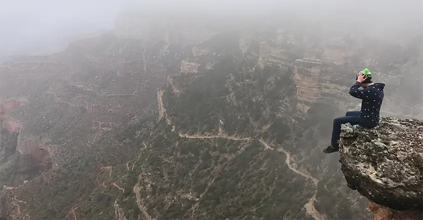 Imagen de joven sentado al borde de un precipicio con unas vistas espectaculares